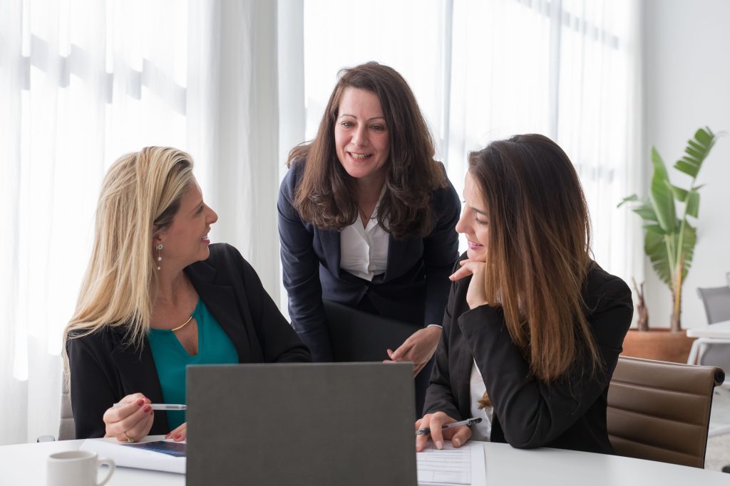 Three women collaborating around a laptop during a leadership session