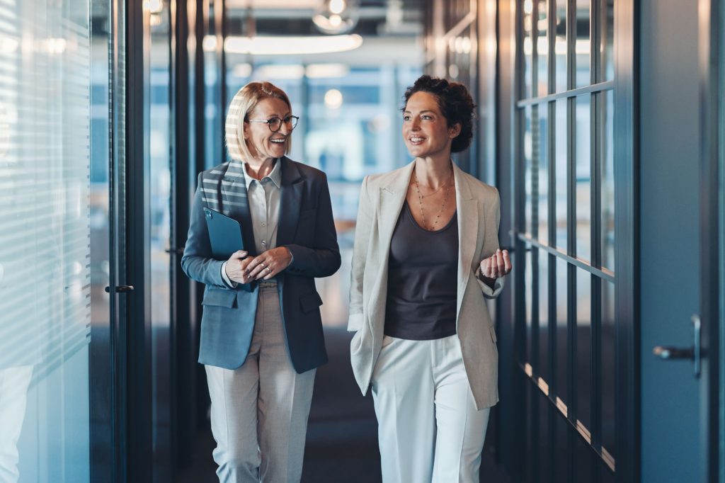 Two women leaders discussing work while walking through a modern office