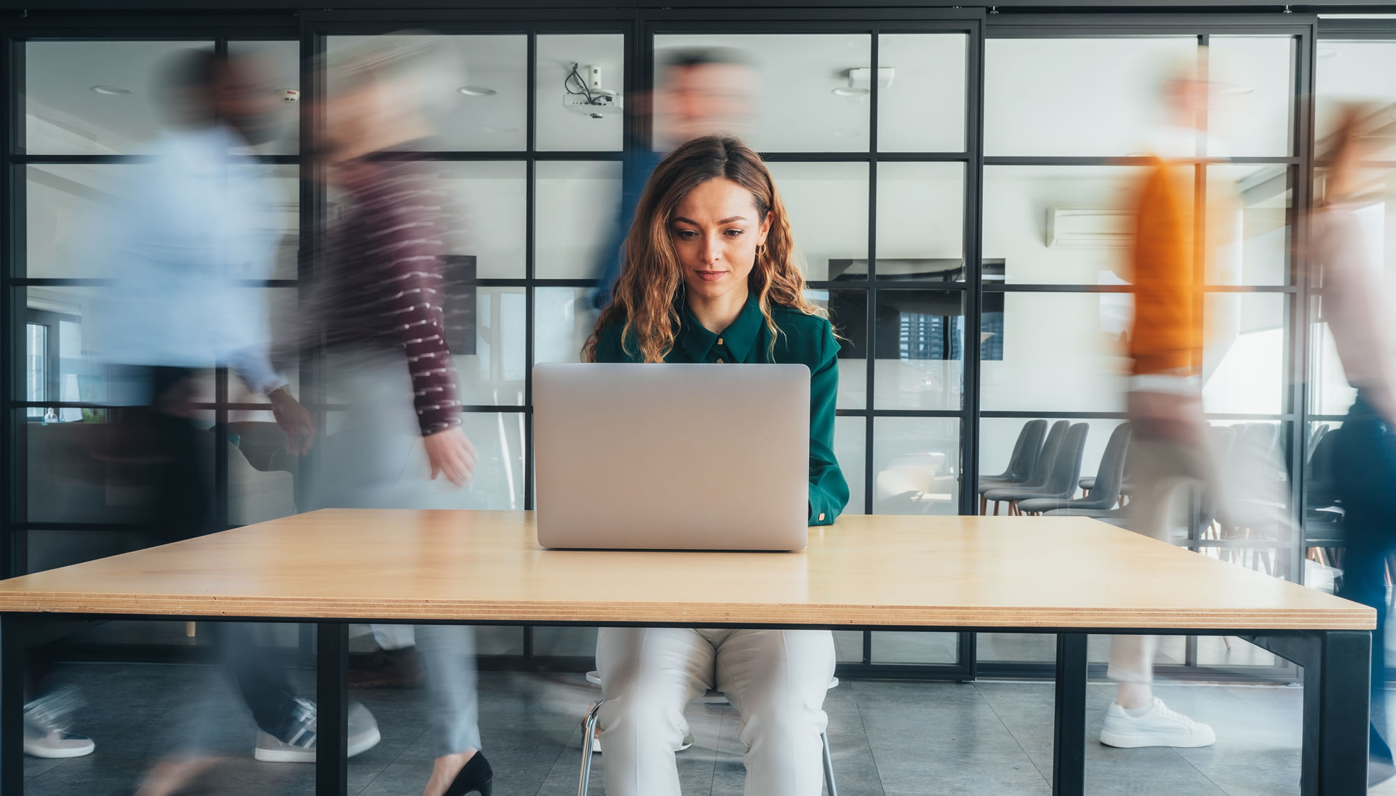 Woman working at a laptop while colleagues move through a busy workplace