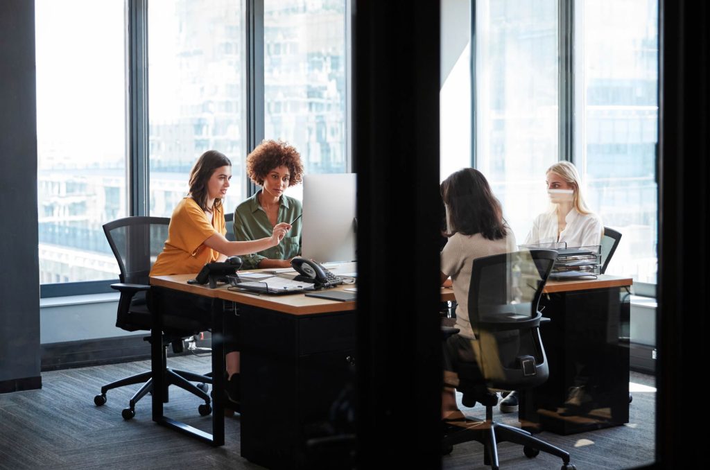 Four women collaborating around a computer in a modern office