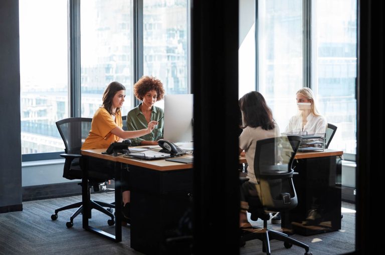 Four women collaborating around a computer in a modern office