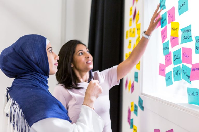 Two women organising ideas on colourful sticky notes during a workshop